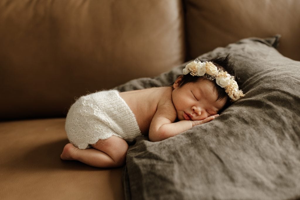 Newborn baby asleep on her tummy with a big flower headband on her head. A balanced accesorie. 