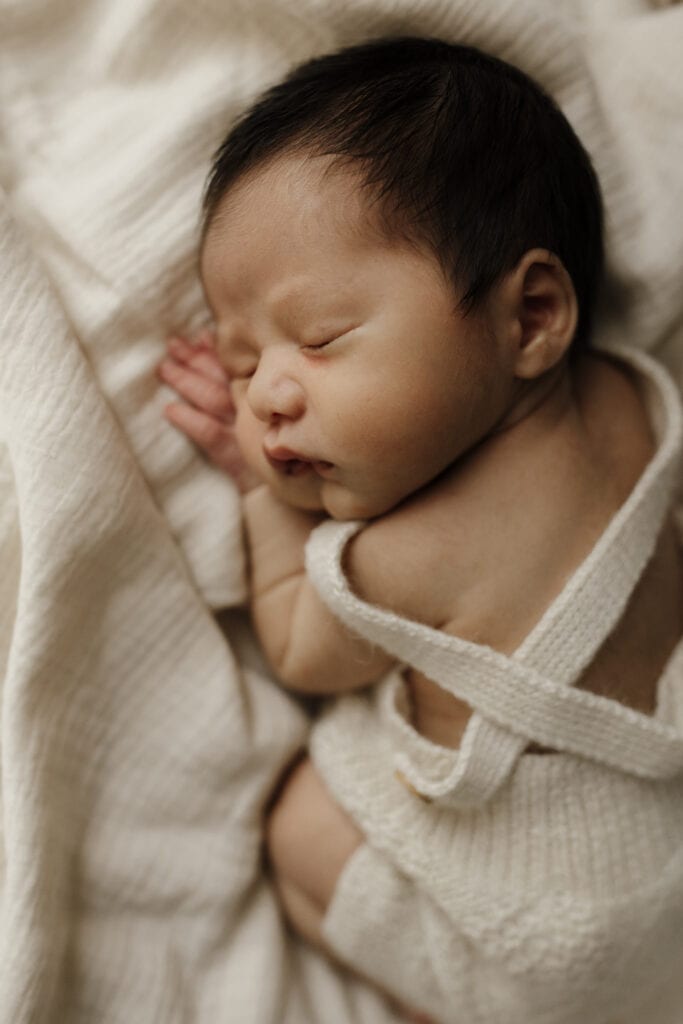 A newborn baby asleep on his tummy in a neutral coloured hand knitted onesie.