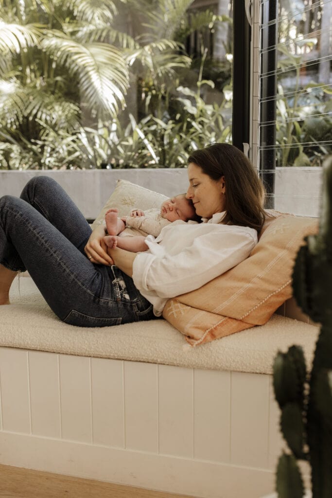 A new mom wearing jeans and a white shirt holding her baby comfortably. 
