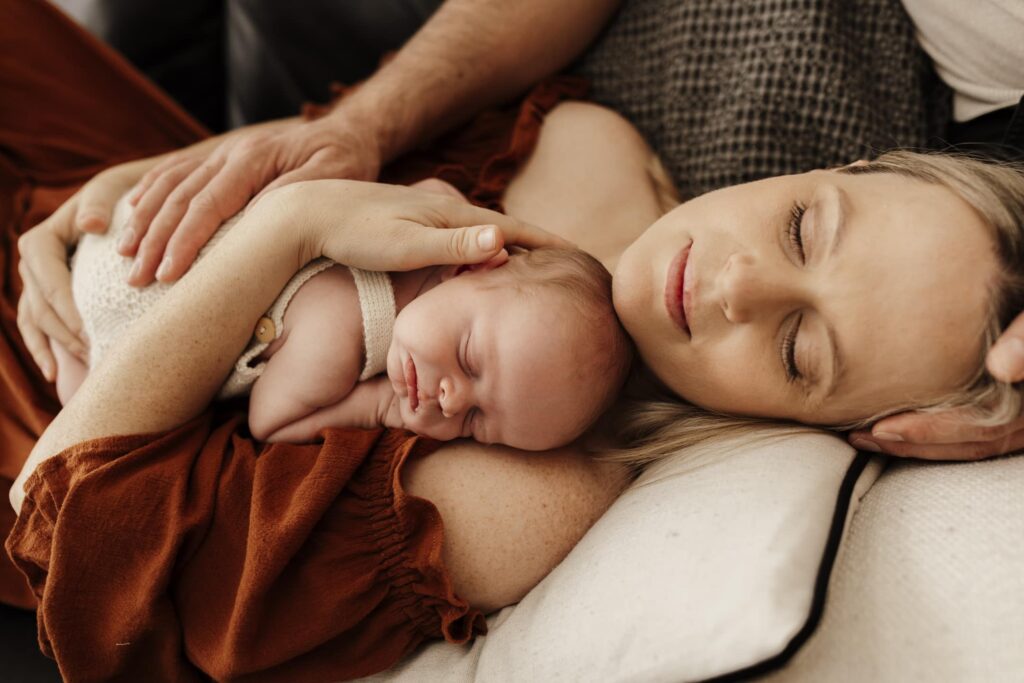 A newborn baby asleep on his mother's chest. Curled up and photographed from the front.