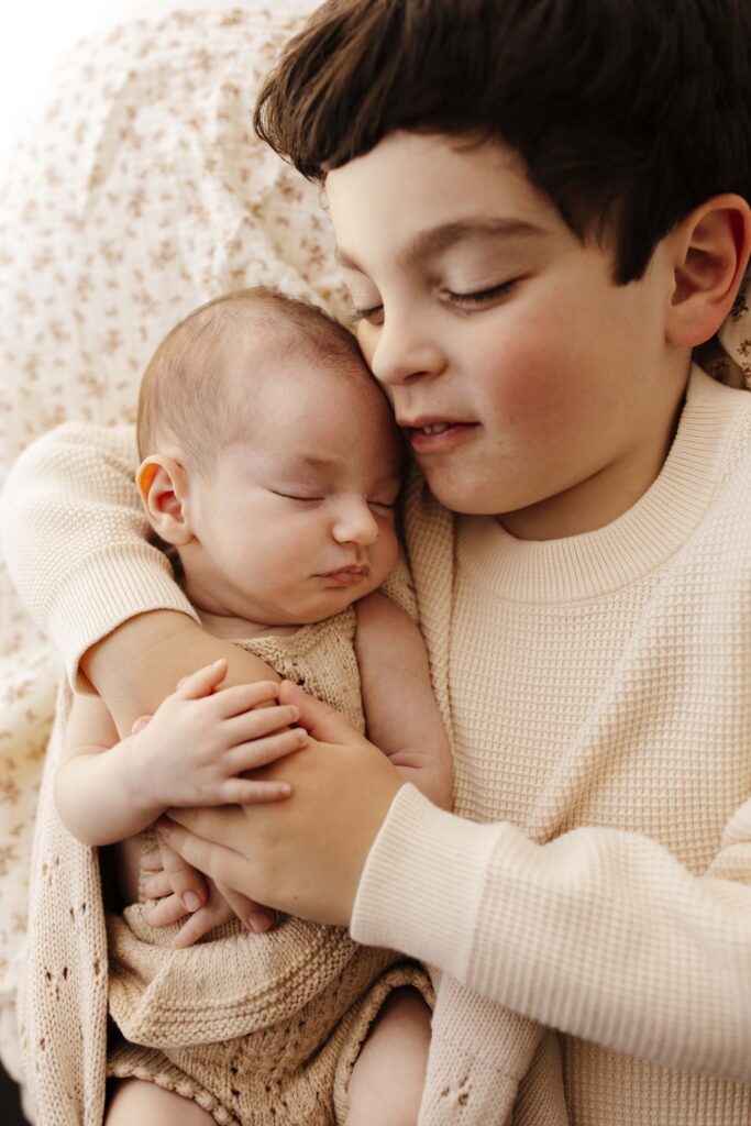 A baby girl cradled in her brothers arms as he smiles.